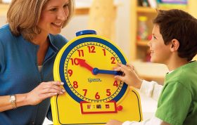 تصویر معلم در حال آموزش ساعت به کودک